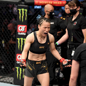 女MMA拳手在UFC八角籠中慶祝勝利，背景有官員。