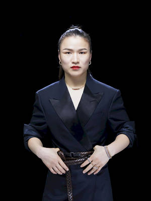 一位身穿黑色西裝外套和辮子腰帶的女性，在攝影棚肖像中嚴肅地擺姿勢。 — 中文 壁紙