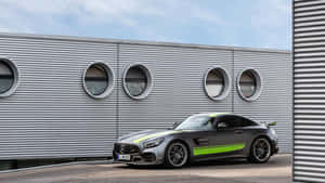 灰色 Mercedes-AMG GT 跑車帶有綠色條紋，停在一個現代金屬建築前。 — 汽車 壁紙