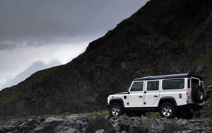 白色 Land Rover Defender 停放在多雲天空下的岩石山地地形上