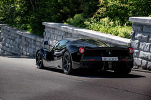 黑色法拉利 LaFerrari 在蜿蜒的山路上，有石牆和綠樹。