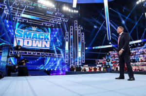 身穿西裝的WWE SmackDown主持人站在摔角擂台邊緣，舞台燈光下。 — 摔角 GIF 壁紙