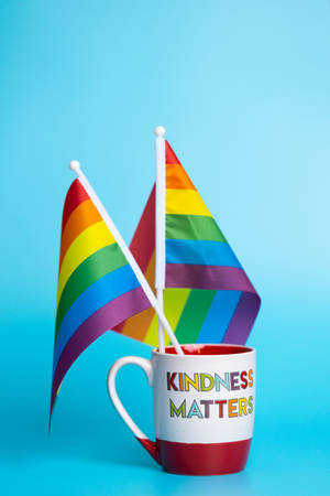 一個寫有 kindness matters 的杯子在藍色背景下舉著兩面彩虹驕傲旗。