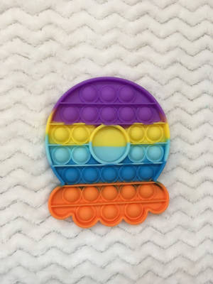 一個彩虹色太陽形狀的Pop-it減壓玩具放在白色絨毛毯上。