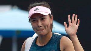 網球運動員微笑著向人群揮手，戴著粉紅色遮陽帽和藍色上衣。 — 網球 壁紙