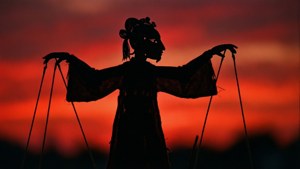 木偶師在紅色夕陽天空下握著線的剪影。