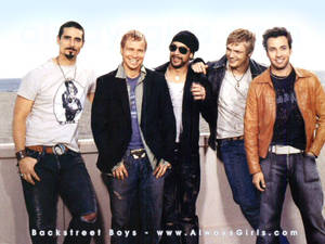 Backstreet Boys 的五位男士穿著休閒服裝在海邊微笑。