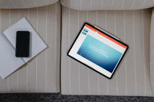 平板電腦在條紋沙發上顯示 PowerPoint 指南，旁邊有電話和筆記本。 — MacBook 壁紙