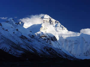 晴朗藍天下，雲彩在山頂周圍飄蕩的雪山山峰。