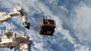 機械臂在地球雲層覆蓋的表面上方捕獲衛星。 — 行星 壁紙