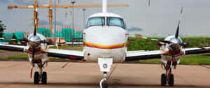 白色雙引擎螺旋槳飛機停泊在建築工地附近的停機坪上。
