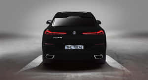 黑色BMW V8X6轎車後視圖，帶有發光的紅色尾燈和照明地面圖案。 — 純黑 壁紙