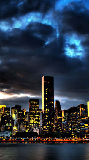城市天際線夜景，帶有發光的窗戶和水面上方的暗色暴風雲。