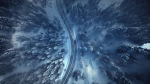從上方看，一輛紅色汽車在冬季森林的雪路上行駛。 — 冬日美學 壁紙