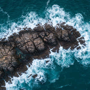 綠松石色的海浪從上方拍打著深棕色的鋸齒狀岩石。 — 電影 GIF 壁紙