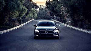 黑色豪華房車在黃昏時分行駛在綠樹成蔭的道路上。