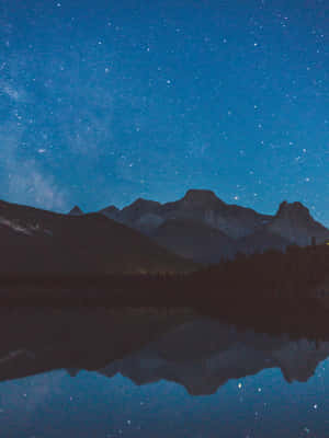 繁星點點的夜空映照在平靜湖面上的山脈
