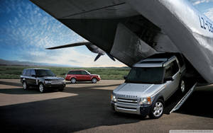 三輛 Land Rover SUV 放置在機場跑道上大型飛機機翼下方及旁邊。