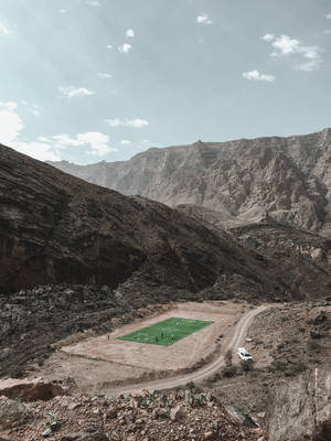 足球運動員在岩石沙漠峽谷的綠色場地上，附近有一條蜿蜒的道路和一輛白色汽車。