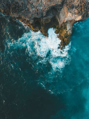 從上方看到的碧綠色海浪拍打黑色岩石懸崖。 — 秋天 壁紙
