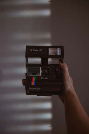 手拿著黑色Polaroid Supercolor相機，後面牆上有光條。