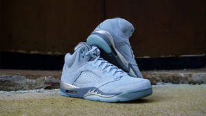 淺藍色麂皮 Air Jordan 5 運動鞋，帶有銀色點綴，放在混凝土階梯上。