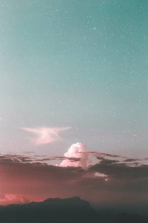 粉紅色和藍綠色的天空，星星和雲朵在黃昏時的山脈輪廓之上。