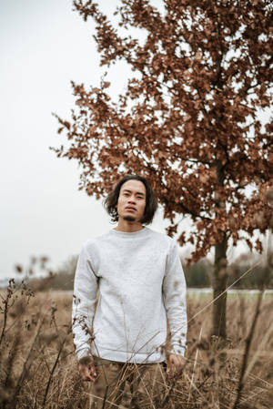 年輕男子站在秋天的田野中，樹下枝葉茂密