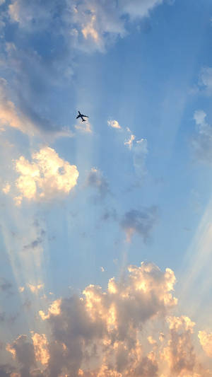 一架飛機在夕陽天空下飛行，伴隨著金色雲彩和陽光。