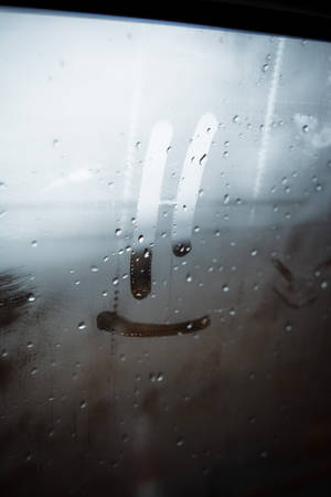 一扇帶有雨滴和畫出笑臉的玻璃門，喚起一種陰鬱的室內場景。 — 鎖屏 壁紙