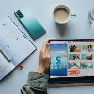 手拿著平板電腦，Microsoft Edge 已打開，旁邊有日曆、電話、咖啡和水在桌子上。