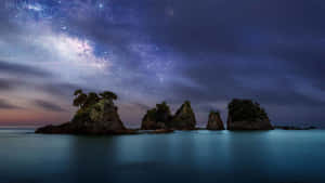夜晚平靜海洋中岩石島嶼上方的銀河星系。