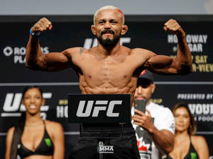 UFC拳手在體重磅上彎曲手臂，身後有兩名女性。