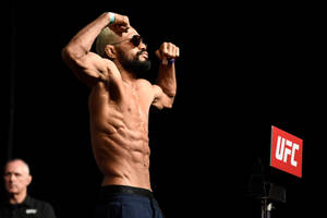 赤裸上身的戰士在紅色標誌的UFC舞台上繃緊肌肉。