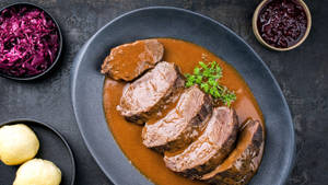 深色碟上的切片牛肉配肉汁和配菜。