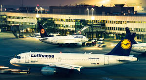 漢莎航空飛機在夜間機場客運大樓，燈光閃爍並帶有動態模糊。