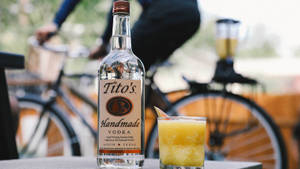 Tito's伏特加酒瓶和橙雞尾酒，背景有騎單車的人。