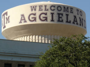 水塔，上面有 'Welcome to Aggieland' 字樣，下方有綠色樹木