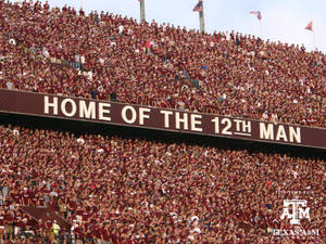球場觀眾身穿栗色球衣在「Home of the 12th Man」標誌下歡呼。