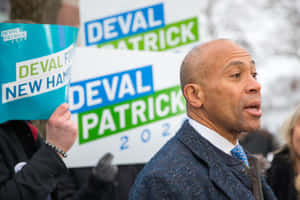 Deval Patrick 在政治集會上手持競選標語發表演說。
