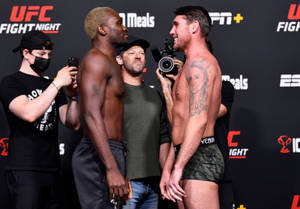 兩位UFC拳手在稱重活動中面對面站立，有攝影師和品牌背景。