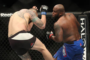 兩名男性MMA拳手在鐵籠內，一人踢向另一人，後者用手臂擋格。