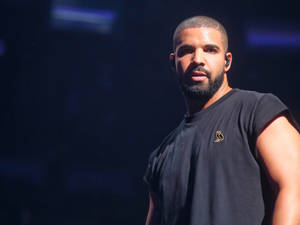 Drake 在舞台上表演，身穿黑色無袖襯衫，搭配藍色舞台燈光。