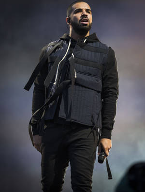 Drake 在舞台上唱歌，穿著黑色絎縫背心和連帽衫。