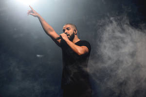 Drake 在煙霧彌漫的舞台上於強光下對著咪高峰唱歌。