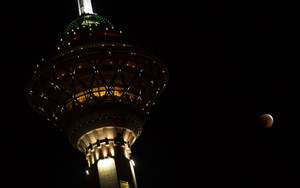 夜間發光的塔，天空中有發光的月亮。 — 夜晚 GIF 壁紙