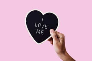 手拿著心形黑板，上面有訊息 I LOVE ME，背景為粉紅色