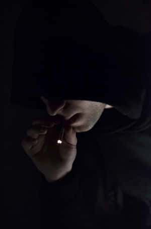 穿著深色連帽衫的人在昏暗光線下點煙