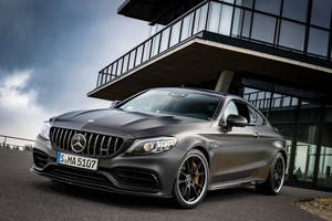 啞光灰色 Mercedes-AMG C63 S 雙門轎跑車停放在現代玻璃建築下。