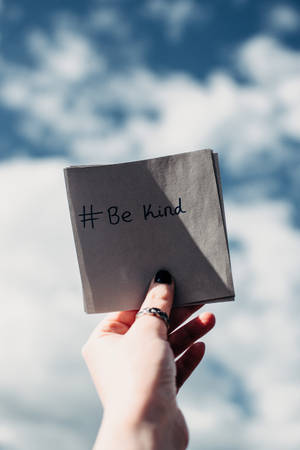 手拿著印有 be kind 訊息的餐巾，背景是藍天